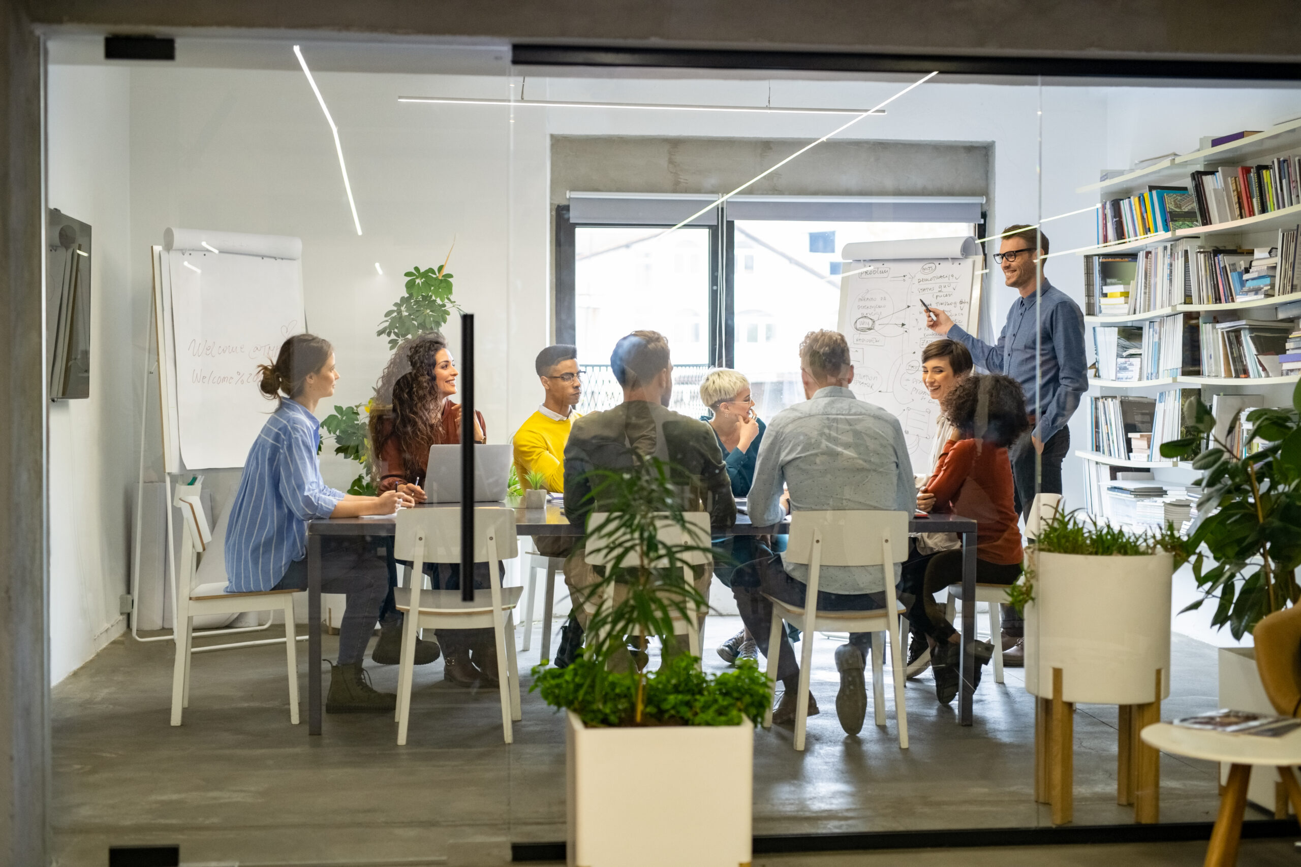 Confident mature businessman giving a presentation to his crative team in office. Business brief with annual goals with casual employees. Happy leadership man training young businessmen and smiling businesswomen sitting at conference table.